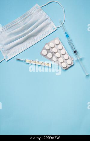 Auf blauem Hintergrund sind Pillen, eine medizinische Maske, ein Thermometer und eine Spritze. Stockfoto