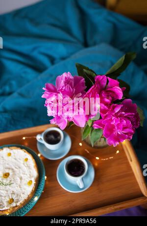 Wunderschöner Vanille-Käsekuchen, Kaffee, blaue Tassen, pinkfarbene Pfingstrosen in einer Glasvase. Stockfoto