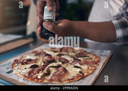 Ein wenig Würzen geht einen langen Weg. Ein unkennbarer Mann steht und bereitet in seinem Restaurant eine frisch zubereitete Pizza zum Mitnehmen zu. Stockfoto