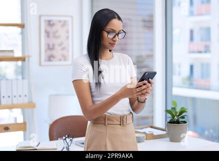 Ich muss auf diese Antwort antworten. Eine attraktive junge Frau, die eine SMS sendet, während sie in ihrem Büro steht. Stockfoto