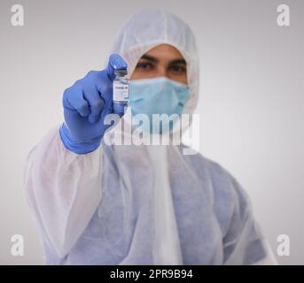 Vertrauen Sie mir, Sie brauchen das. Ein Arzt, der in einem Einweg-Hazmat-Anzug steht und eine Ampulle für den Covid-Impfstoff hält. Stockfoto