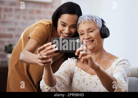 Tippen Sie hier, um ein Selfie zu machen. Eine ältere Frau benutzt ein Smartphone, um Selfies mit ihrer Tochter zu Hause zu machen. Stockfoto