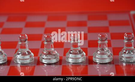 Stücke von transparentem Schach, Bauern. Transparente Schachfiguren auf Schachbrett, roter Ton. Stockfoto