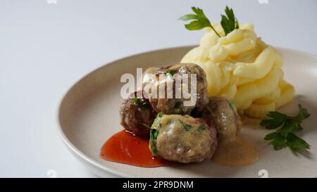 Ein Teller mit schwedischen Fleischbällchen mit Kartoffelpüree, traditioneller cremiger Soße und Preiselbeere. Stockfoto