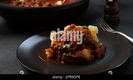 Rindereintopf mit Tomatensauce, Gewürzen und Kräutern auf Kartoffelpüree. Stockfoto