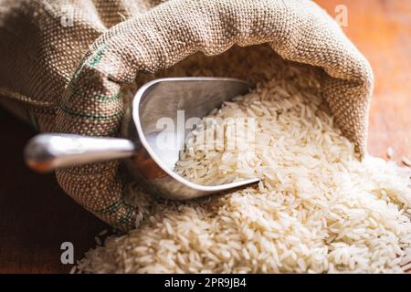 Ungekochter weißer Reis in einem Leinensack auf einem Holztisch. Stockfoto