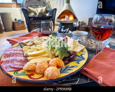 Nahaufnahme von Wurstplatte und Gläsern Rotwein auf einem bunten Teller im Wohnzimmer. Stockfoto