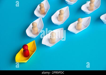 Rote Holzfigur auf gelbem Papierschiff Origami führt den Rest an. Stockfoto