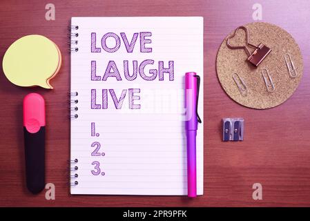 Textzeichen mit „Love Laugh Live“. Geschäftsübersicht Be inspired positive joy your days Laching guter Humor Notizbuch mit wichtigen Nachrichten am Schreibtisch mit Bürobedarf. Stockfoto