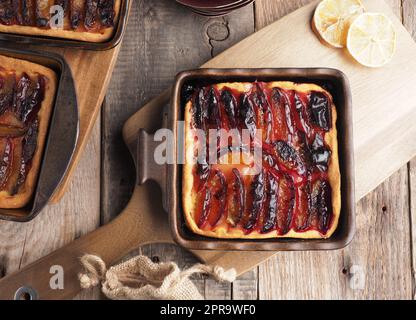 Frisch gebackener Pflaumenkuchen in Keramikschüsseln auf einem rustikalen Küchentisch Stockfoto