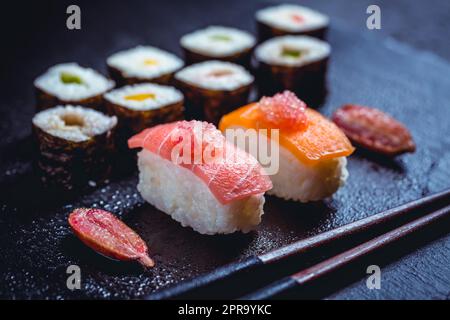 Auswahl an veganem Sushi mit Gemüse, Seitan, Konjakpflanze, Tofu als Fischersatz, mit Fingerkalk als Kaviar auf Schwarz Stockfoto