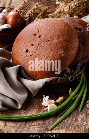 Zwei frische Brotlaibe mit rustikalen Naturelementen auf Tonplatte auf dem Tisch. Stockfoto