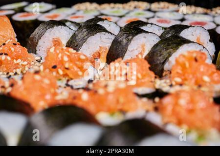 Nahaufnahme von Futomaki-Brötchen mit verschiedenen Füllungen serviert mit Sesamsamen. Stockfoto