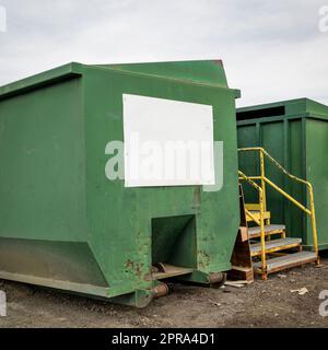 Grüner Industriecontainer aus Stahl mit einem weißen Blankoschild am Recyclingzentrum Stockfoto