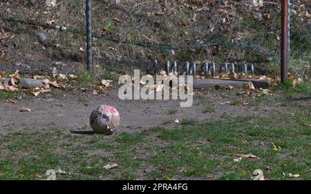 Der alte dreckige Football liegt auf dem verlassenen Spielplatz. Teile des alten Zauns, Pfosten und Tors sind sichtbar und zeigen den verlassenen Zustand des Ortes. Stockfoto