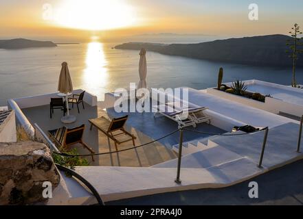 Sonnenliegen auf der Terrasse im Dorf Imerovigli mit herrlichem Blick auf den Sonnenuntergang über der Caldera in Santorin Stockfoto