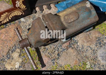 Ein alter Schraubstock steht auf einem gepflasterten Boden. Stockfoto