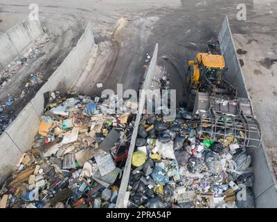 Radlader, der auf Mülldeponien eingesetzt wird, Abfallmaterial mit einer Schaufel transportiert und entsorgt, Luftaufnahme aus einem großen Winkel. Stockfoto