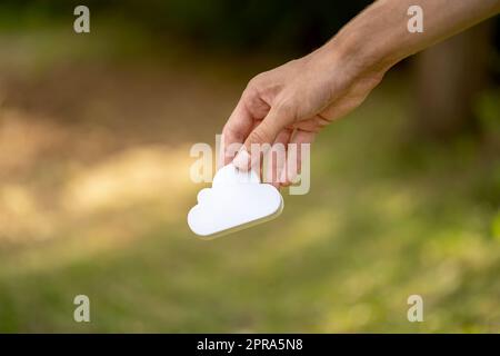 Mann mit einem einfachen weißen Wolkensymbol in der Hand, Cloud-Computing- und Speicherservice-Schild in der Hand, isoliertes Objekt, verschwommener Hintergrund, Copy Spa Stockfoto