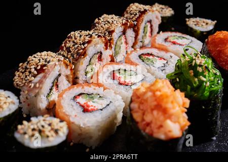 Japanische Küche. Nahaufnahme köstlicher Sushi-Brötchen mit verschiedenen Füllungen auf dunklem Hintergrund. Stockfoto