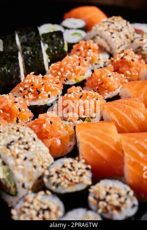 Nahaufnahme einer Reihe von Sushi-Gattungen mit rohem Lachs und Sesamsamen. Stockfoto