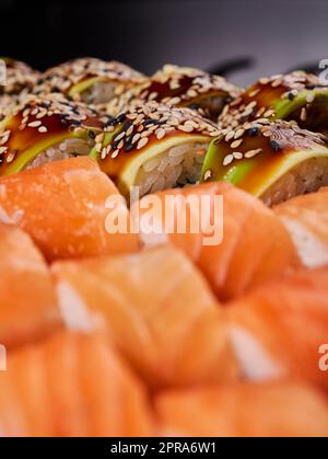 Nahaufnahme von Sushi-Brötchen mit Avocado-Scheiben und kalifornischer Brötchensoße in einem verschwommenen Vordergrund. Stockfoto