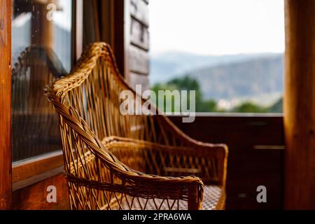 Elemente von dekorativen Möbeln. Nahaufnahme einer Korbbank auf dem Balkon einer Holzhütte. Stockfoto