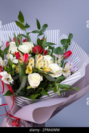 Nahaufnahme eines leuchtenden Straußes aus weißen Rosen, bunten Iris und roten Tulpen. Stockfoto