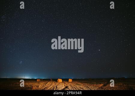 Nächtlicher Sternenhimmel Über Haystacks Im Sommer-Agrarfeld. Nachtsterne Über Der Ländlichen Landschaft Mit Heuballen Nach Der Ernte. Landwirtschaftliches Konzept Stockfoto