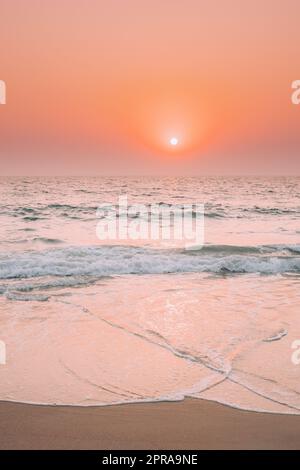 Sonnenuntergang Sonne Glanz Über Meer. Natürlicher Sonnenaufgang Himmel Warme Farben Über Dem Wellenmeer. Meerwasser Schaum Spritzer Waschen Sandstrand Stockfoto