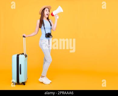 Glückliche junge Frau mit Gepäck und hält Megaphon isoliert auf gelbem Hintergrund, Sommer, Reisekonzept. Stockfoto