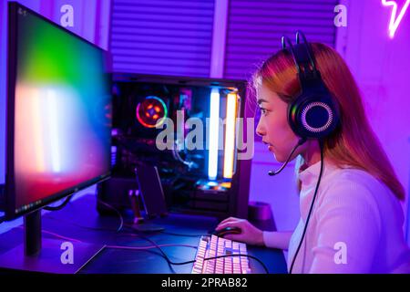 Asiatischer Profi-Gamer, der Online-Videospiele auf einem Desktop-PC spielt, verfügt über farbenfrohe Neon-LED-Lichter Stockfoto