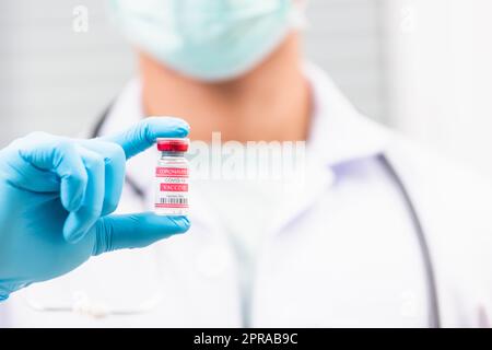 Wissenschaftler in Uniform, der eine Gesichtsmaske trägt und den Coronavirus-Impfstoff zeigt Stockfoto