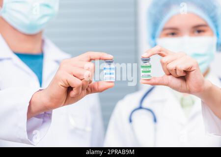 Ärztin oder Wissenschaftlerin in Uniform trägt eine Gesichtsmaske, die den Coronavirus-Impfstoff zeigt Stockfoto