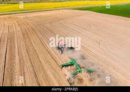 Luftaufnahme. Pflügen Des Traktors. Beginn Der Landwirtschaftlichen Frühjahrssaison. Kultivator, gezogen von Einem Traktor in ländlicher Ackerlandschaft. Staub Steigt Unter Dem Pflug Auf Stockfoto