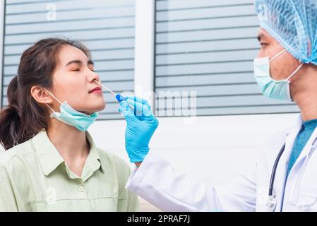 Doktor man nehmen Speichelprobe durch die Nase mit Wattestäbchen, um Coronavirus-Test von einer jungen asiatischen Frau zu überprüfen Stockfoto