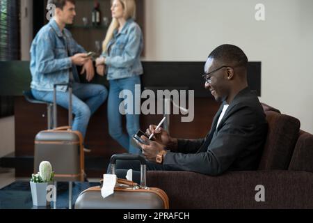 Geschäftsmann, der an einem Tablet-PC arbeitet, während er in der Flughafenlounge auf seinen Flug wartet. Stockfoto