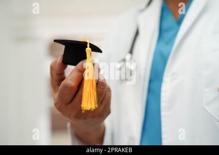 Asiatische Frau Arzt hält Abschlusshut im Krankenhaus, Medizinische Ausbildung Konzept. Stockfoto