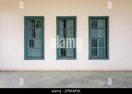 Weiße Wand mit drei grünen Fensterläden aus Grunge-Holz, schmiedeeisernen Barren und Marmorboden Stockfoto