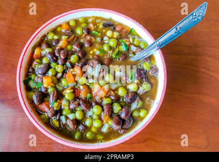 Gemüseschüssel Suppe mit Bohnen Erbsen Kartoffeln Zwiebeln Tomaten und Knoblauch in einer weiß rosa Teller Schüssel mit Gabel oder Löffel in Mexiko. Stockfoto