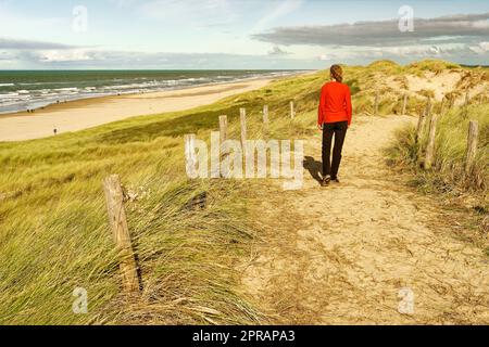 Eine Frau, die auf einem wunderschönen sandigen Pfad am Meer spaziert. North Holland Dune Reserve, Egmond aan Zee, Niederlande. Stockfoto