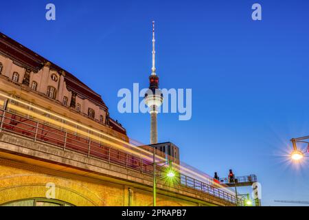 Der ikonische Fernsehturm in Berlin in der Abenddämmerung mit einem bewegungsunscharfen Pendlerzug Stockfoto