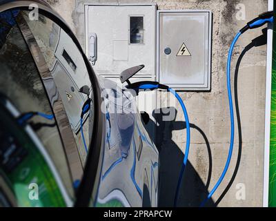 Elektrofahrzeug oder Elektrofahrzeug an der Ladestation mit angeschlossenem Netzkabel auf verschwommener Natur mit blauem Enegy Power-Effekt. Umweltfreundliches Konzept für nachhaltige Energie. Stockfoto