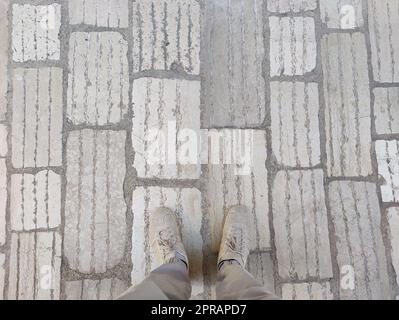 Von oben nach unten: Männerbeine in grauen Hosen und beigen Turnschuhen auf kopfsteingepflasterter Straße. Speicherplatz auf Hintergrund kopieren. Stockfoto