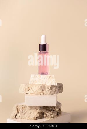 Kosmetische Tropfflasche aus Rosa Glas auf beigen Travertinsteinen auf hellgelber Nahaufnahme Stockfoto