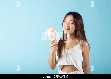 Eine junge asiatische Schönheit, die einen pinkfarbenen tragbaren elektrischen Mini-Ventilator in der Nähe ihres Gesichts hält Stockfoto