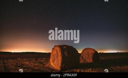 Meteor und Comet Neowise C2020 F3 in Night Starry Sky über Heuhaufen auf dem landwirtschaftlichen Sommerfeld. Nachtstars Über Der Ländlichen Landschaft Mit Heuballen Nach Der Ernte Stockfoto