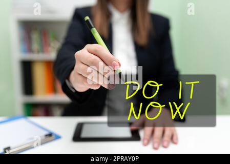 Handschriftlicher Text „Do IT Now“. Aufgeschriebenes Wort Antworten Sie sofort etwas muss sofort erledigt werden Geschäftsfrau hat Tablet am Schreibtisch und zeigt mit Pen auf neue Ideen. Stockfoto