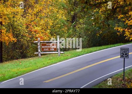 Neben dem Highway befindet sich ein Schild mit Holzrahmen und dem Warriors Path State Park. Es ist von Herbstlaub umgeben. Stockfoto