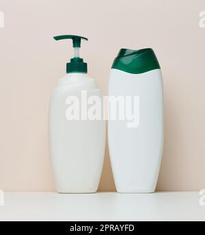 Weiße Plastikflaschen mit einer Pumpe für Shampoo, Duschgel auf beigem Hintergrund Stockfoto